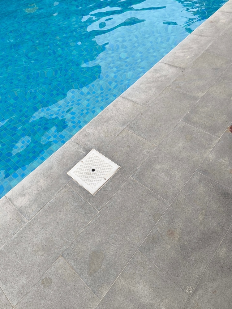 Bordure de Piscine en Pierre Grise et Eau Bleue Bordure de piscine en pierre grise avec couvercle de skimmer blanc et eau bleue mosaïque.