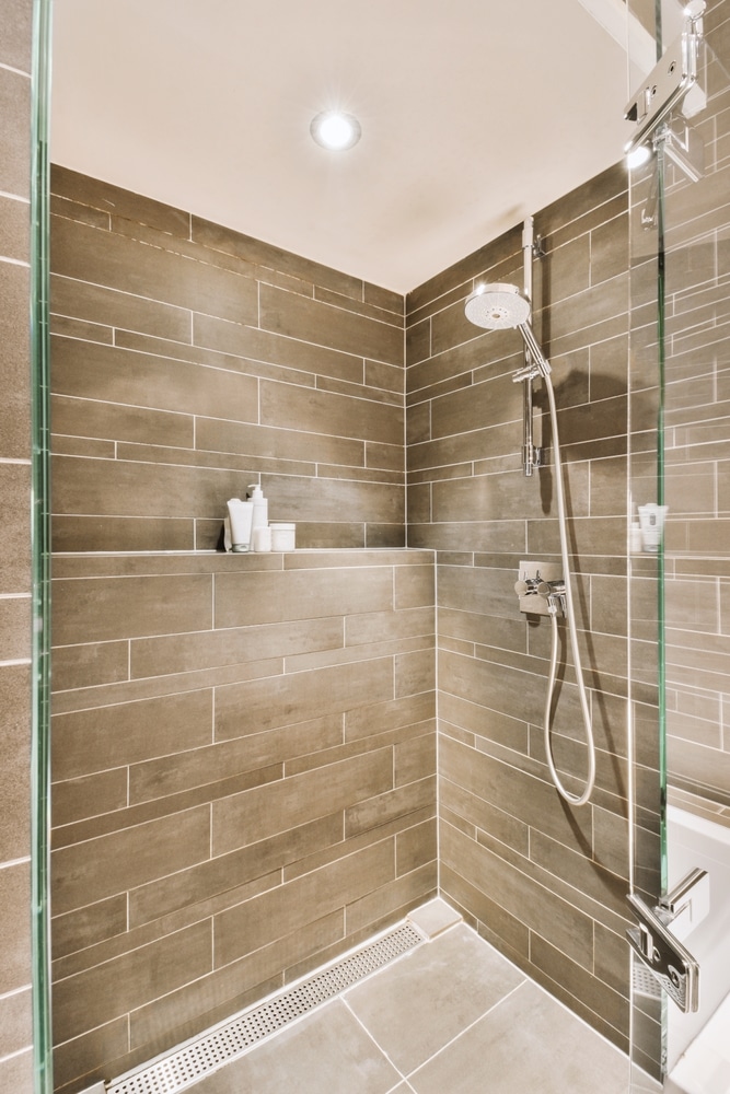 Douche Italienne Moderne : Carrelage Gris et Paroi Vitrée Douche moderne avec carrelage gris brun, paroi vitrée et caniveau de douche linéaire.
