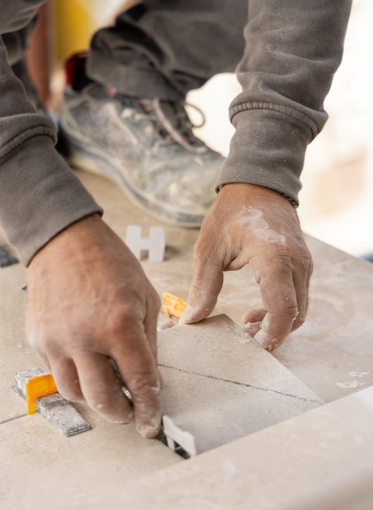 Pose de Carrelage Professionnelle : Guide et Techniques Mains d'un artisan carreleur ajustant un carreau de sol avec des cales et croisillons de nivellement.