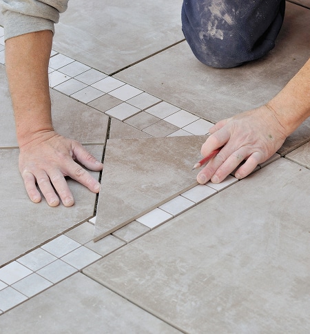 Pose de Carrelage au Sol : Techniques et Marquage Précis Artisan marquant un carreau de sol en grès cérame avec un crayon rouge pour une pose en diagonale avec frise.