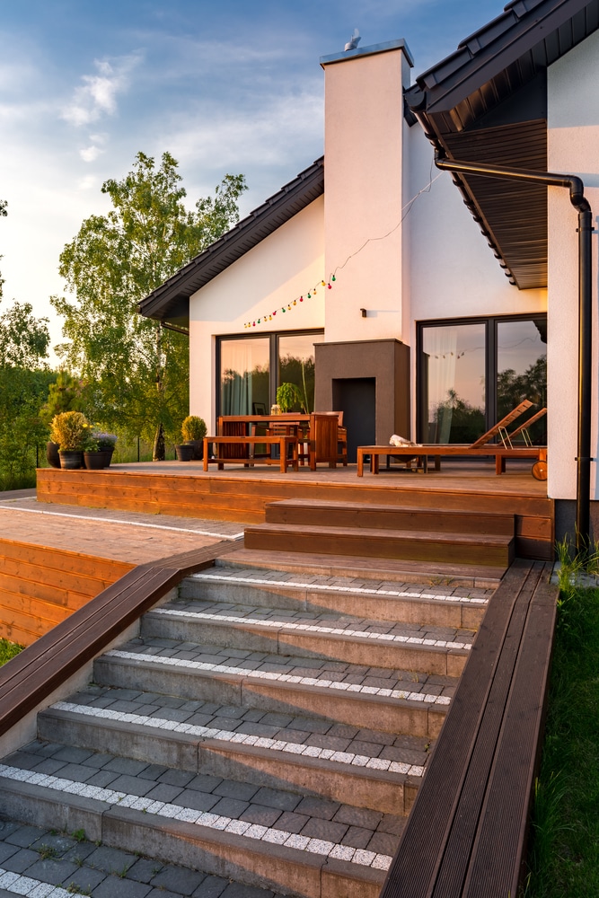 Terrasse Moderne avec Mobilier Bois et Maison Blanche Terrasse moderne avec mobilier en bois, escalier en pierre et maison blanche au coucher du soleil.