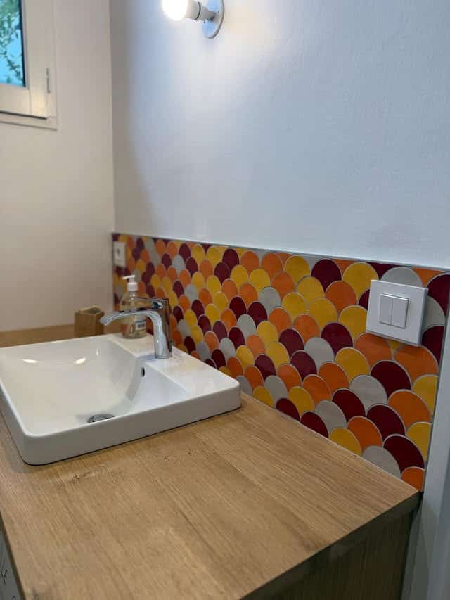 Crédence en mosaïque écailles colorées pour salle de bain Vasque blanche sur plan de travail en bois avec crédence en mosaïque d'écailles colorées rouge et jaune.
